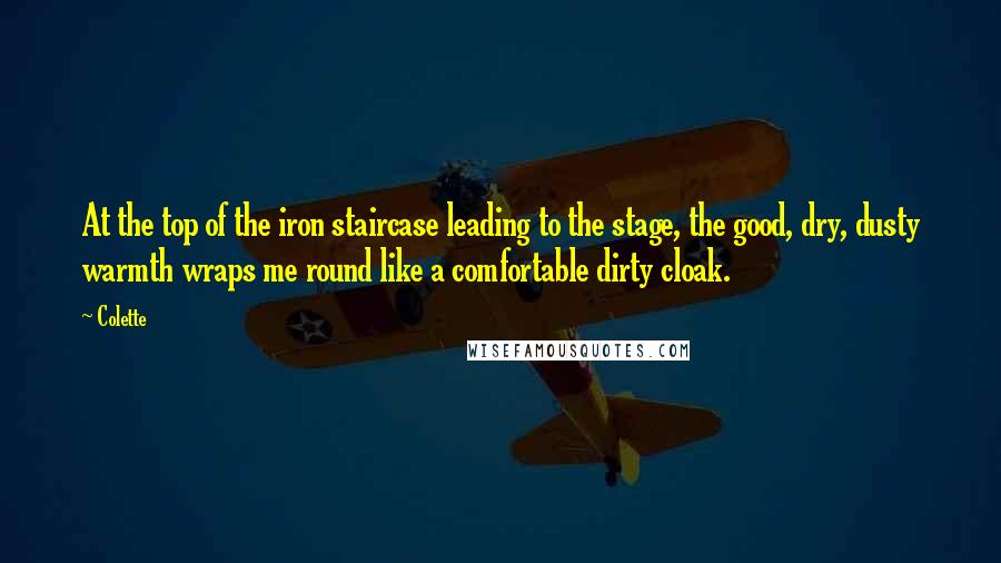 Colette Quotes: At the top of the iron staircase leading to the stage, the good, dry, dusty warmth wraps me round like a comfortable dirty cloak.