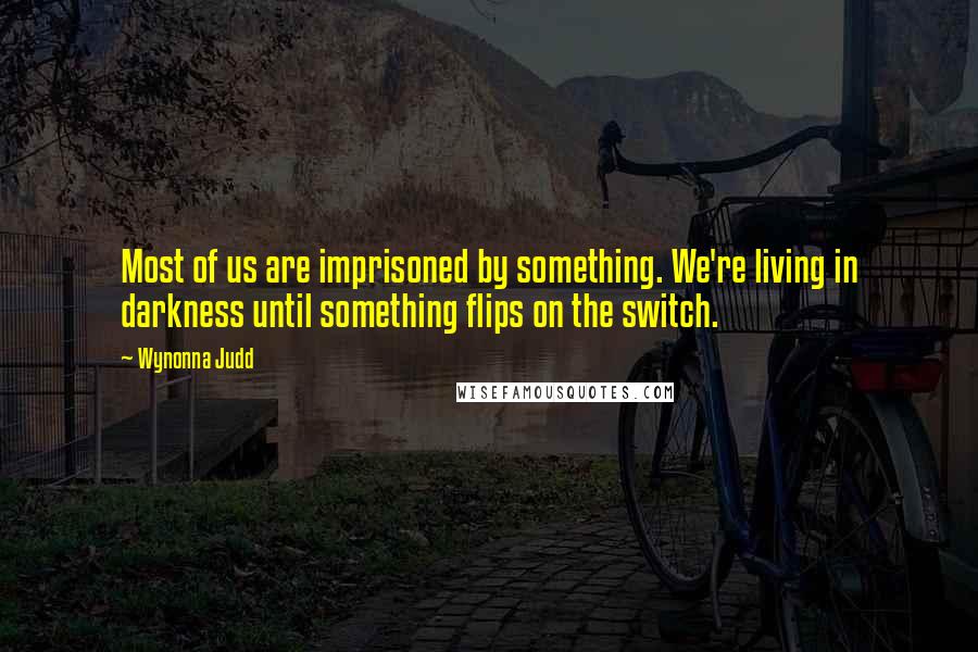 Wynonna Judd quotes: Most of us are imprisoned by something. We're living in darkness until something flips on the switch.