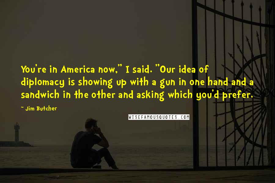 Jim Butcher Quotes: You're in America now," I said. "Our idea of diplomacy is showing up with a gun in one hand and a sandwich in the other and asking which you'd prefer.