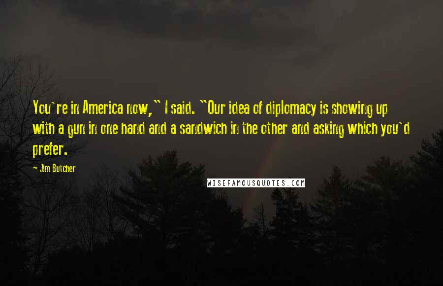 Jim Butcher Quotes: You're in America now," I said. "Our idea of diplomacy is showing up with a gun in one hand and a sandwich in the other and asking which you'd prefer.