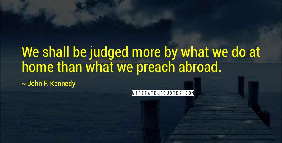 John F. Kennedy Quotes: We shall be judged more by what we do at home than what we preach abroad.