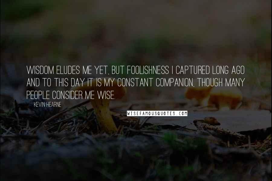 Kevin Hearne Quotes: Wisdom eludes me yet, but foolishness I captured long ago and to this day it is my constant companion, though many people consider me wise.