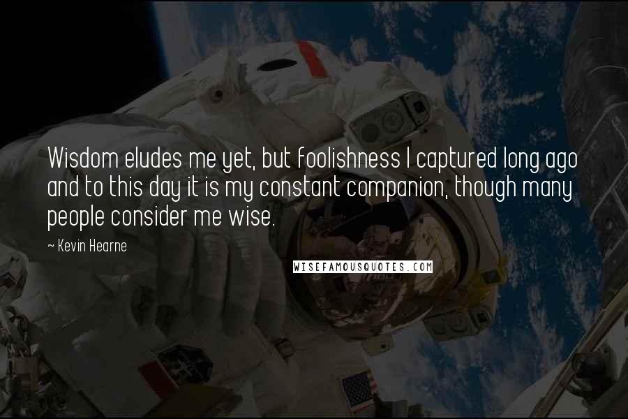 Kevin Hearne Quotes: Wisdom eludes me yet, but foolishness I captured long ago and to this day it is my constant companion, though many people consider me wise.