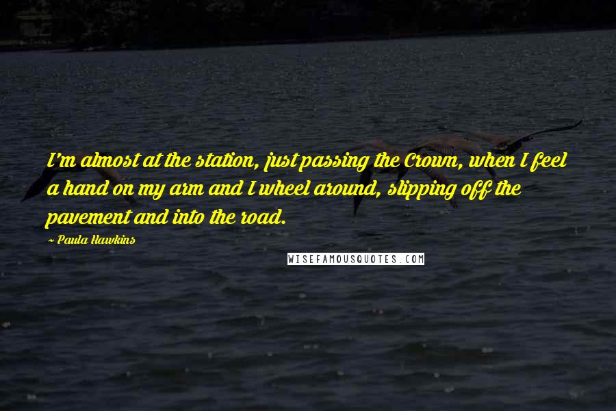 Paula Hawkins Quotes: I'm almost at the station, just passing the Crown, when I feel a hand on my arm and I wheel around, slipping off the pavement and into the road.