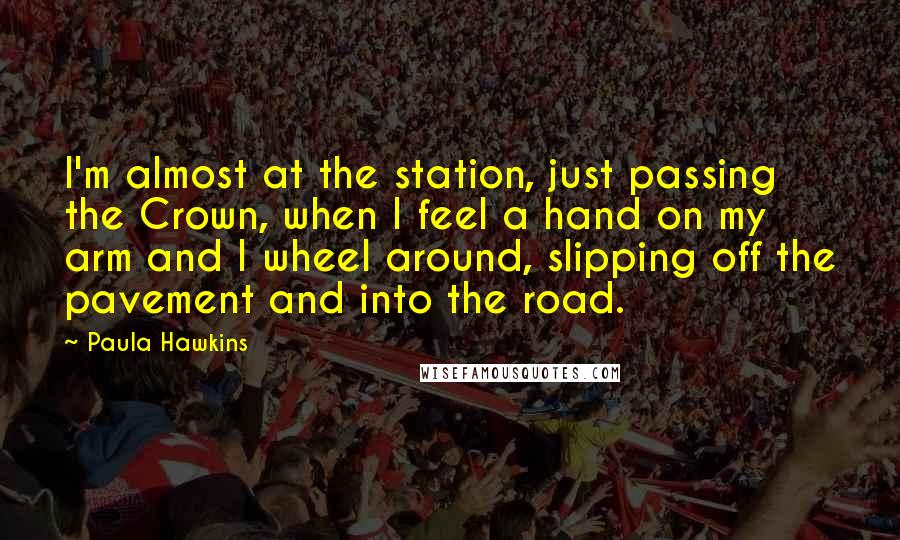 Paula Hawkins Quotes: I'm almost at the station, just passing the Crown, when I feel a hand on my arm and I wheel around, slipping off the pavement and into the road.