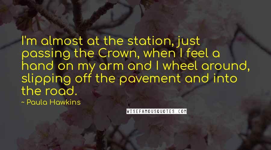 Paula Hawkins Quotes: I'm almost at the station, just passing the Crown, when I feel a hand on my arm and I wheel around, slipping off the pavement and into the road.