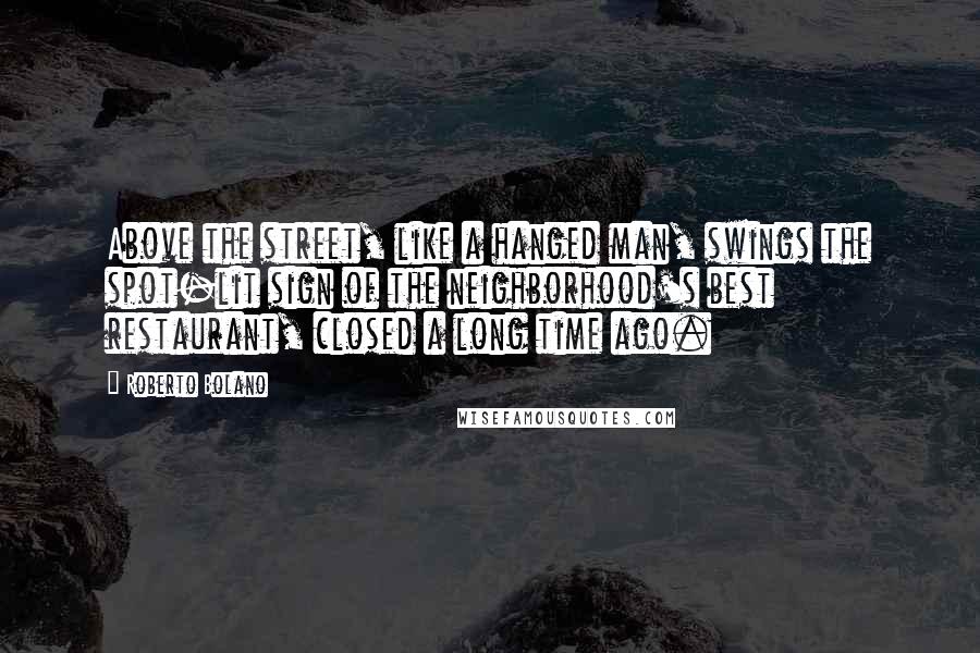 Roberto Bolano Quotes: Above the street, like a hanged man, swings the spot-lit sign of the neighborhood's best restaurant, closed a long time ago.