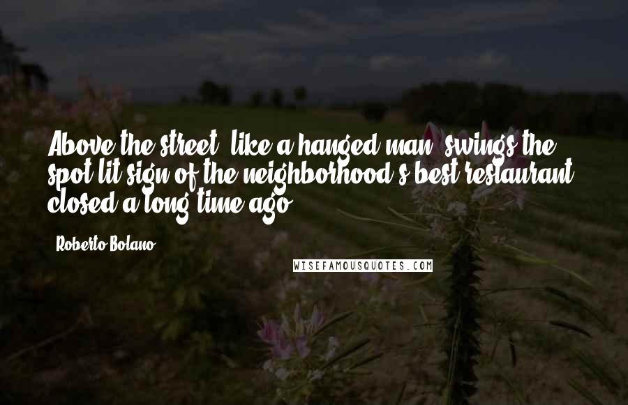 Roberto Bolano Quotes: Above the street, like a hanged man, swings the spot-lit sign of the neighborhood's best restaurant, closed a long time ago.