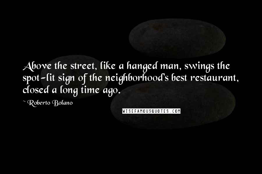 Roberto Bolano Quotes: Above the street, like a hanged man, swings the spot-lit sign of the neighborhood's best restaurant, closed a long time ago.