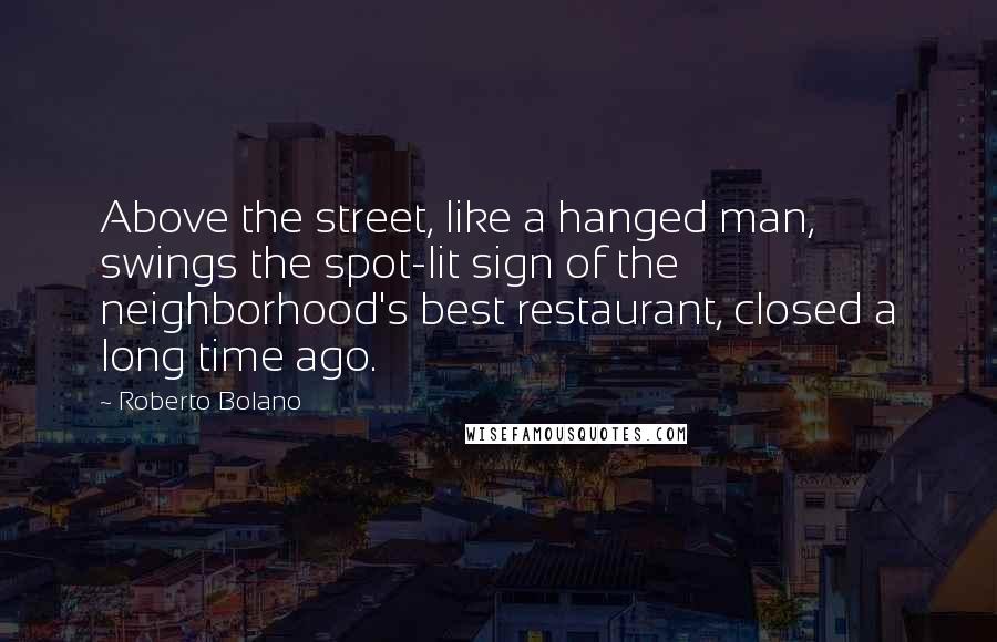 Roberto Bolano Quotes: Above the street, like a hanged man, swings the spot-lit sign of the neighborhood's best restaurant, closed a long time ago.