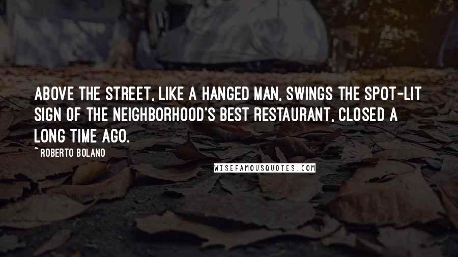 Roberto Bolano Quotes: Above the street, like a hanged man, swings the spot-lit sign of the neighborhood's best restaurant, closed a long time ago.