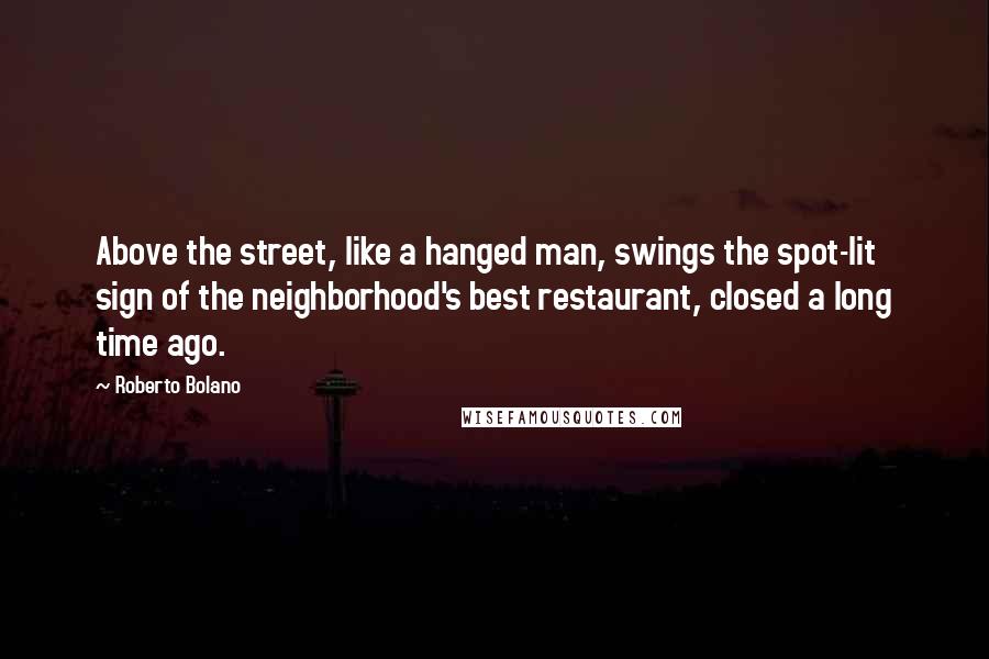 Roberto Bolano Quotes: Above the street, like a hanged man, swings the spot-lit sign of the neighborhood's best restaurant, closed a long time ago.