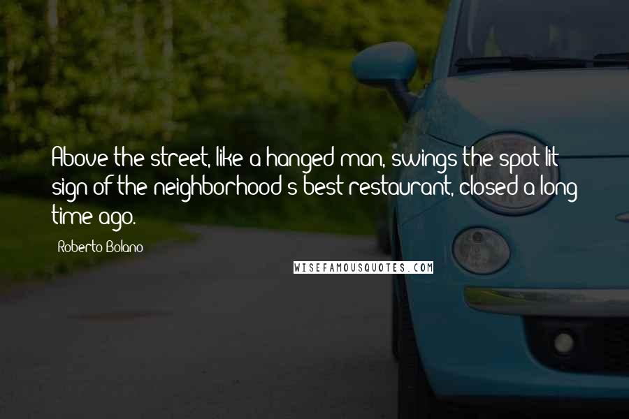 Roberto Bolano Quotes: Above the street, like a hanged man, swings the spot-lit sign of the neighborhood's best restaurant, closed a long time ago.