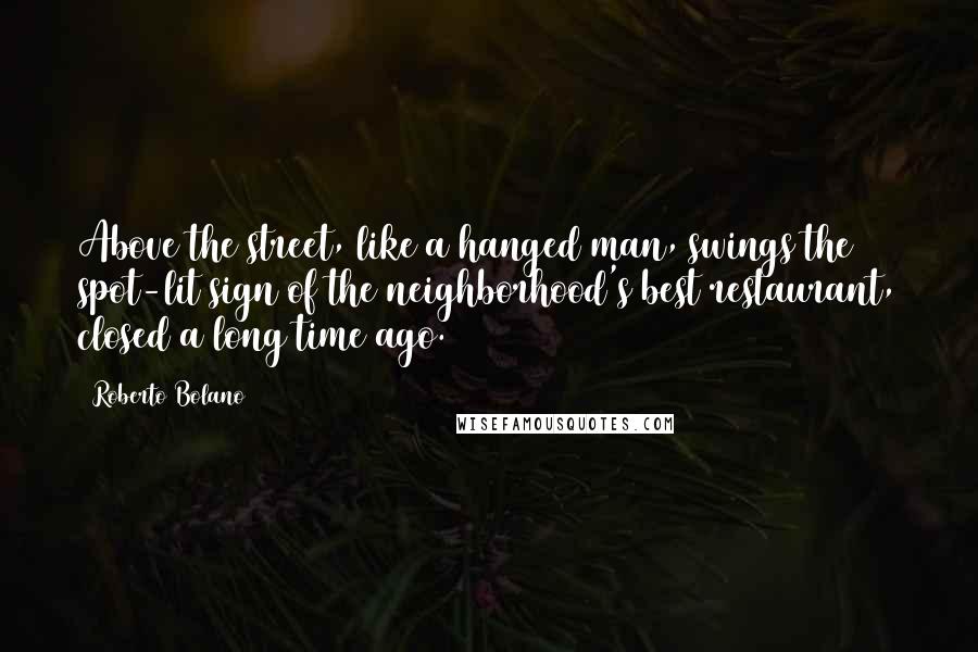 Roberto Bolano Quotes: Above the street, like a hanged man, swings the spot-lit sign of the neighborhood's best restaurant, closed a long time ago.